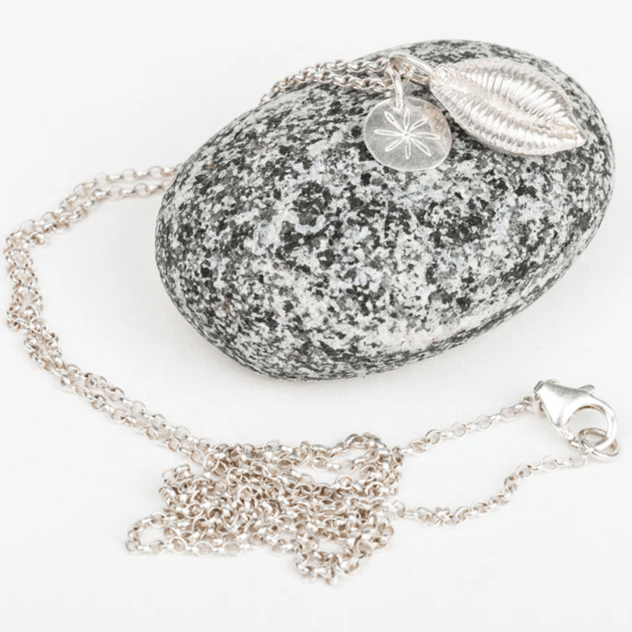 Silver pendant cowrie shell necklace with on a gray speckled pebble stone
