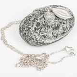 Silver pendant cowrie shell necklace with on a gray speckled pebble stone