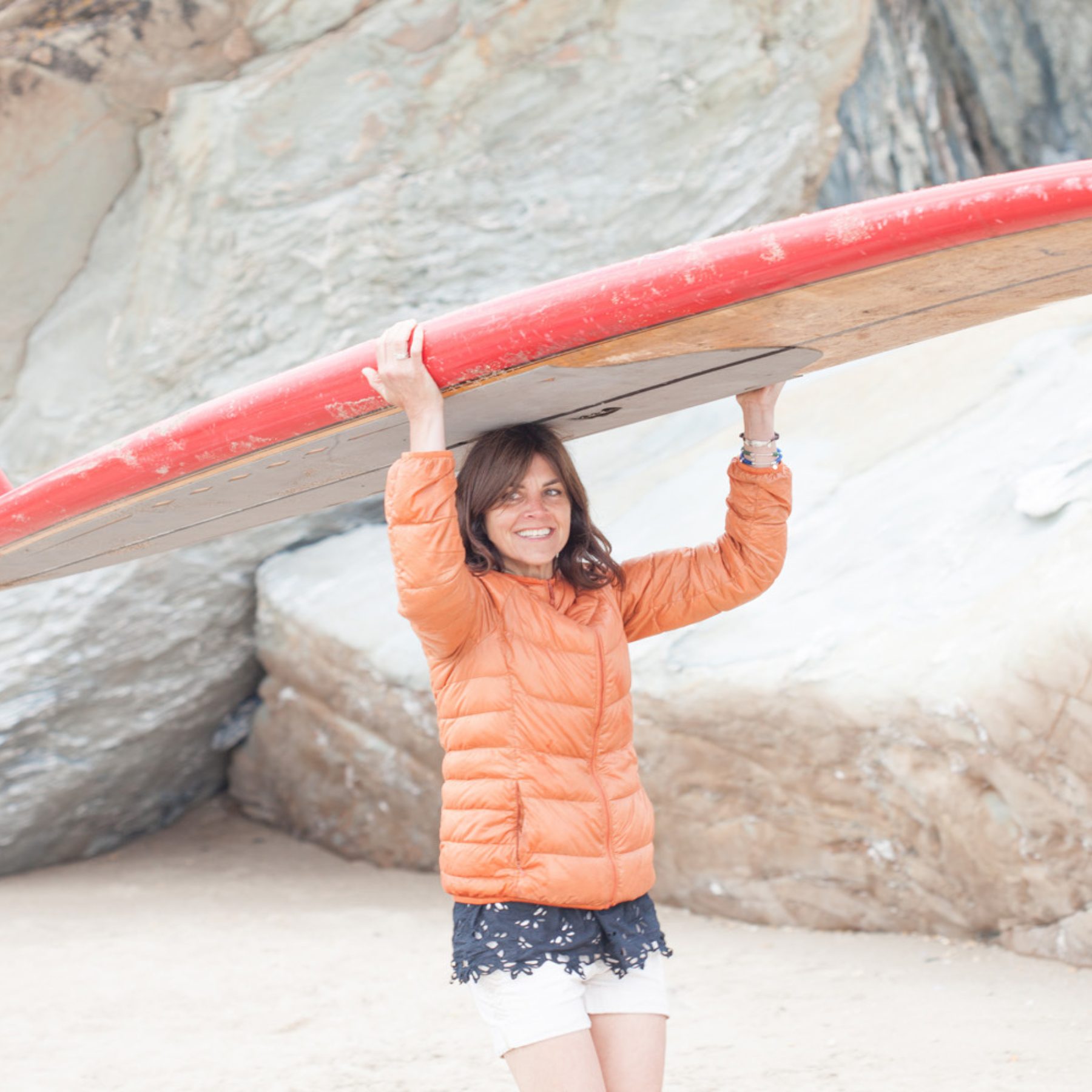 Helen Butler carrying a surfboard on the beach, reflecting the coastal inspiration behind Helen Butler Designs handmade silver jewellery