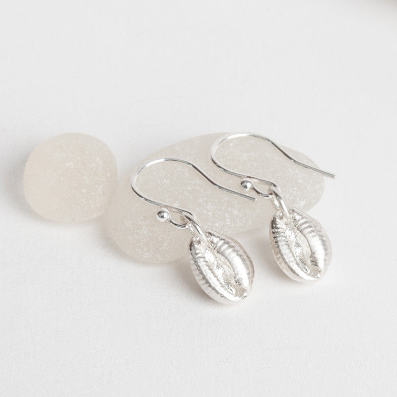 A pair of silver dangle earrings featuring a cowrie shell design, displayed against a neutral background.